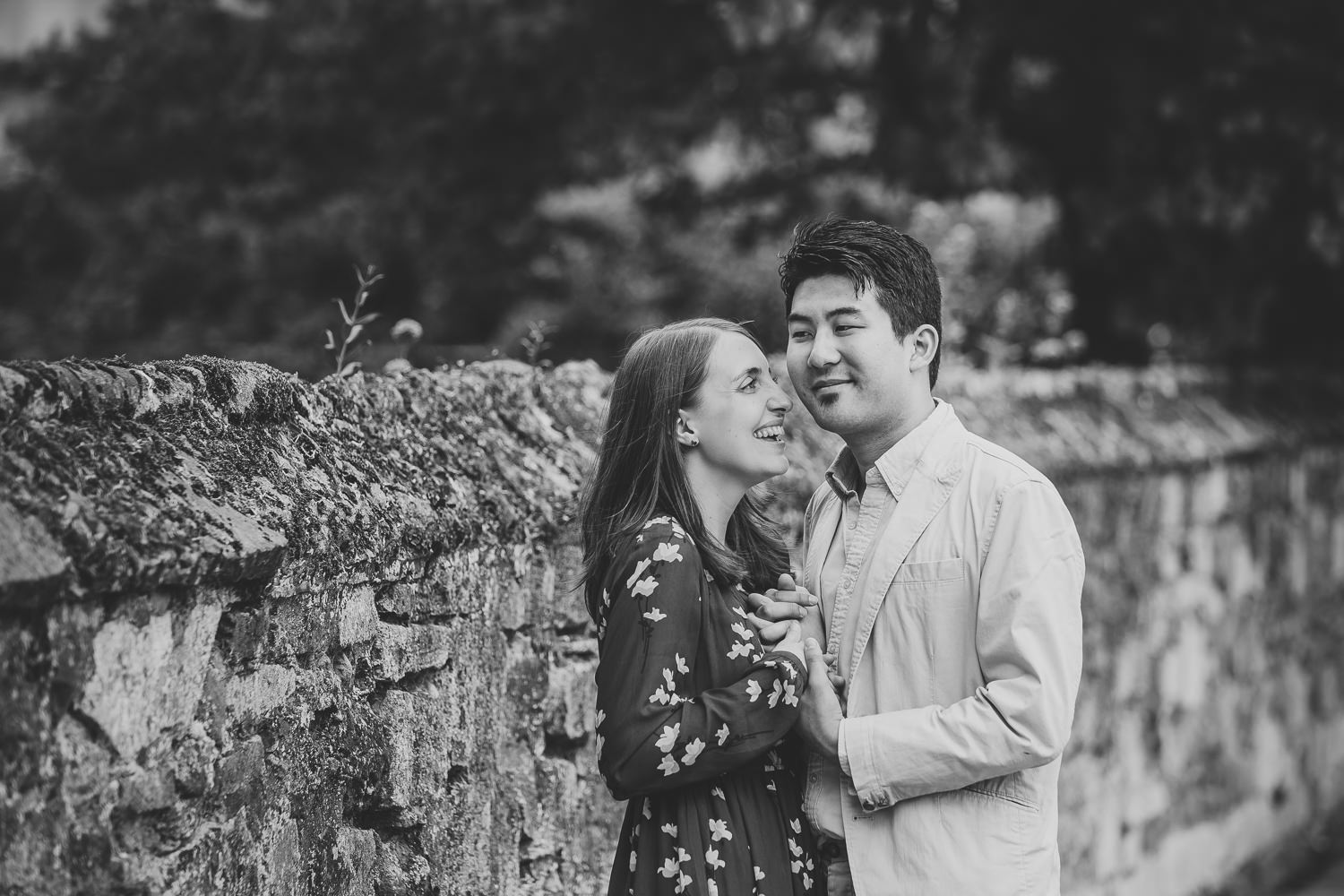 Black and white photo of engaged couple in Ely. Photographed by Ely Photographer. Couple standing by a stone wall.