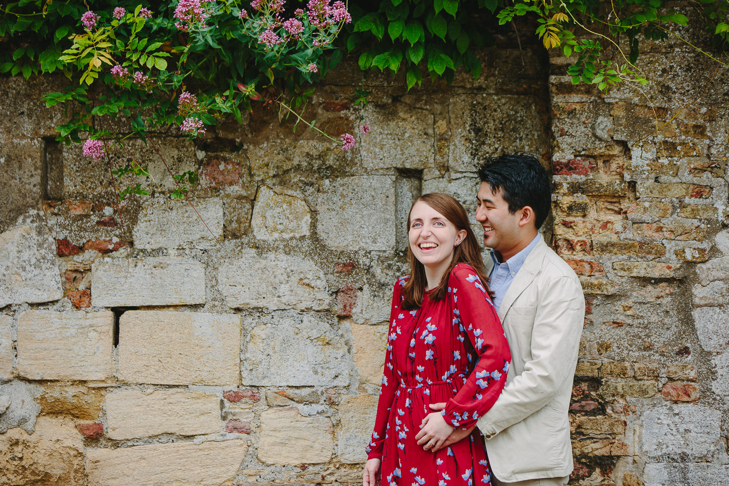 Engaged couple in Ely, photographed by Ely Photographer. Couple standing by a stone wall and pink flowers