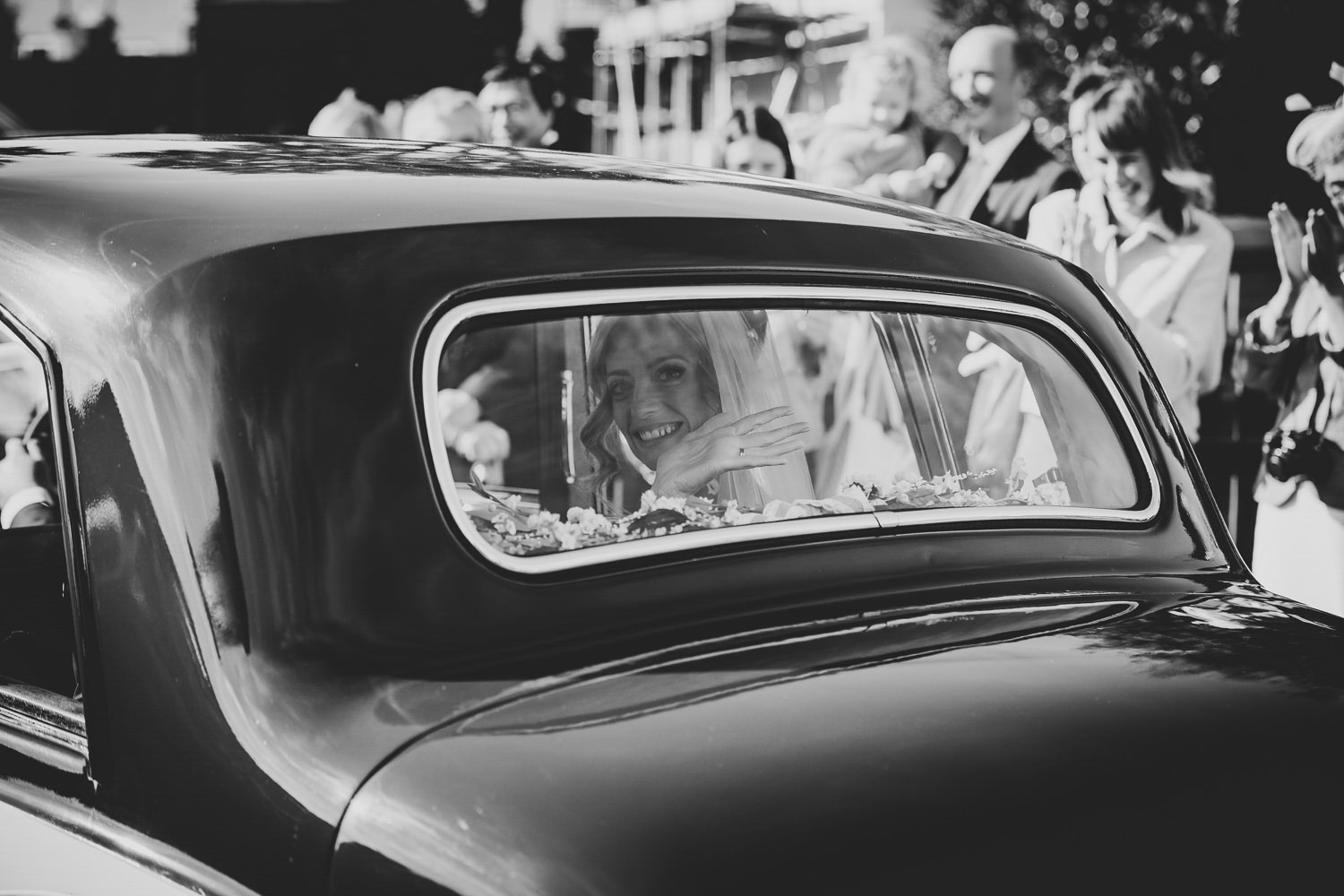 Bride smiling and waving from the rear window of a car
