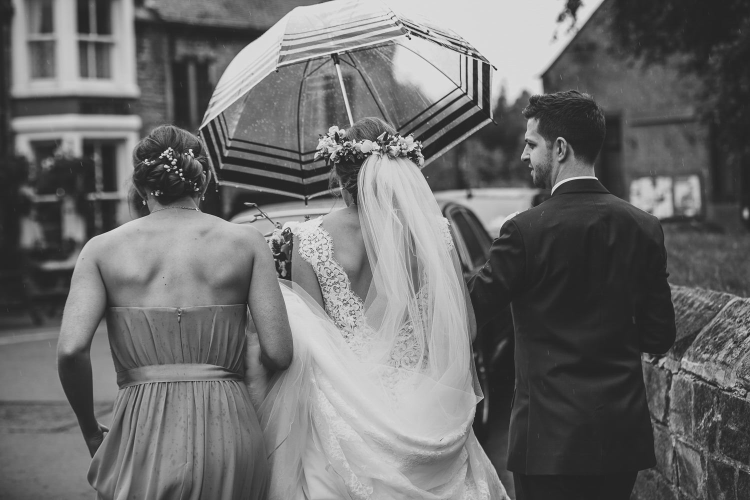 Bride, groom, bridesmaid walking away away, umbrella