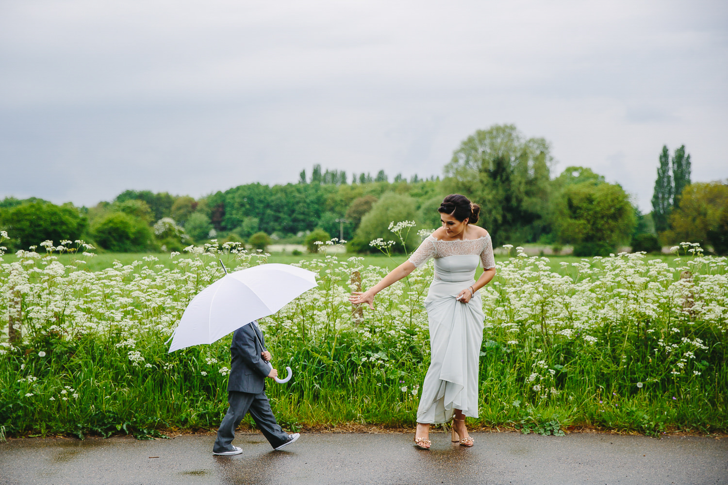 Bride walking in front of page boy with umbrella