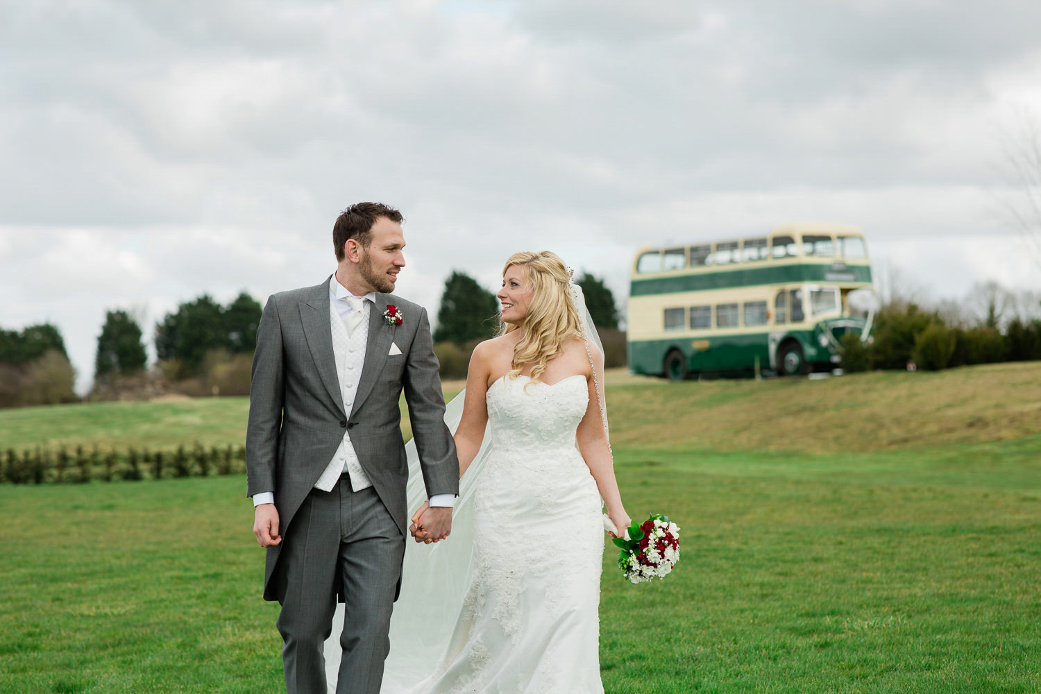 Bride and groom walking on grass with a green bus in the background