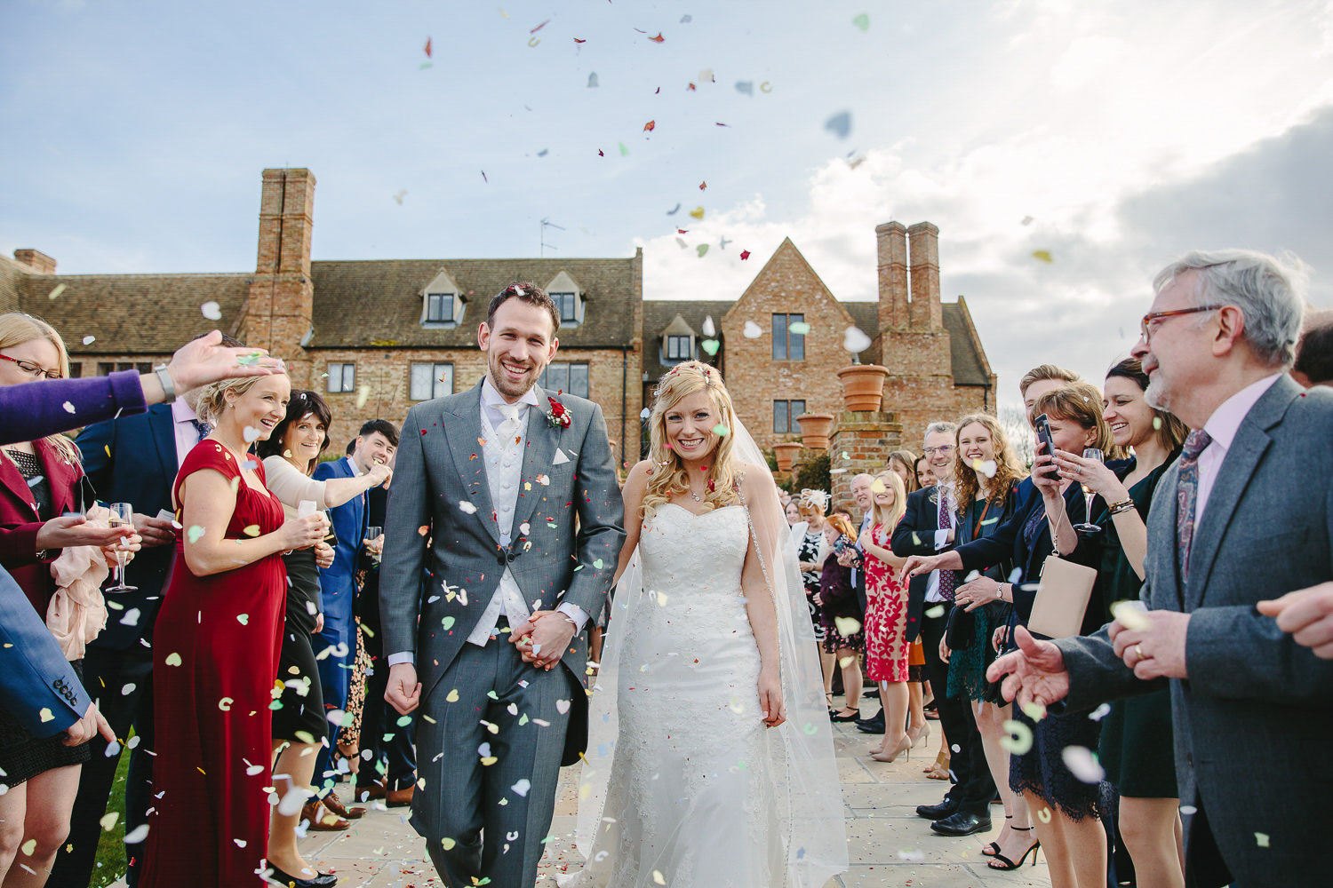 Bride and groom at the Old Hall Ely walking through confetti.