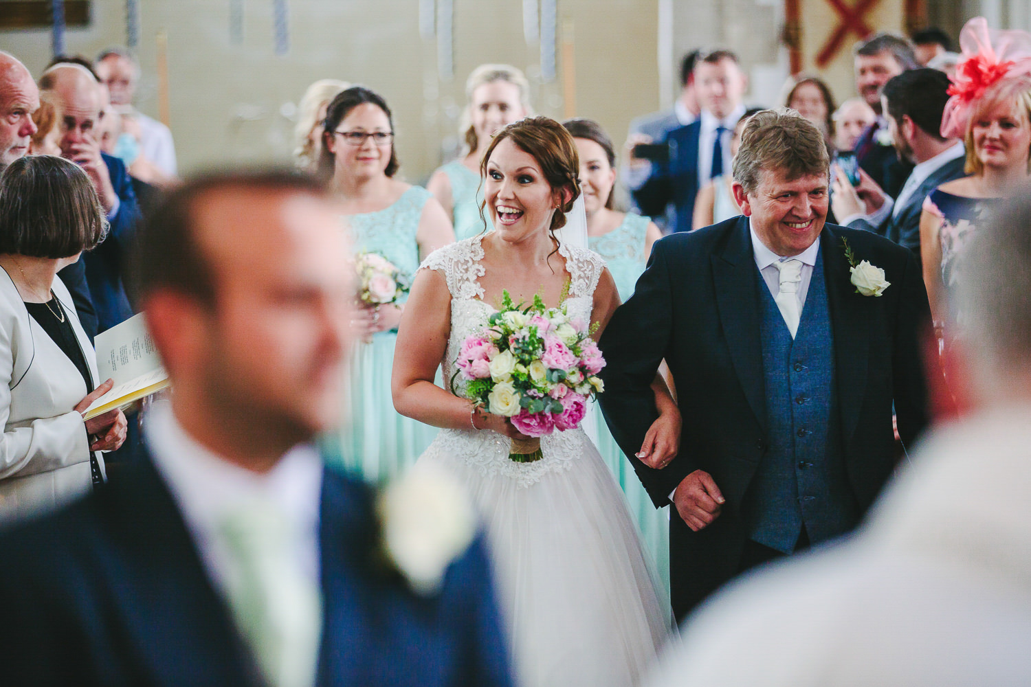 Brides smiling, walking down aisle with father