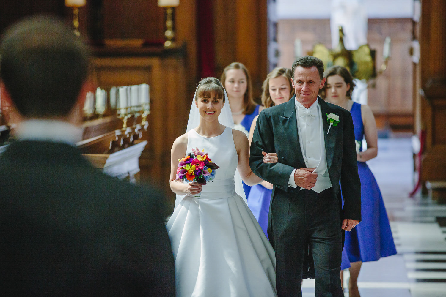 Bride, father and bridesmaids walk down the aisle at Trinity College
