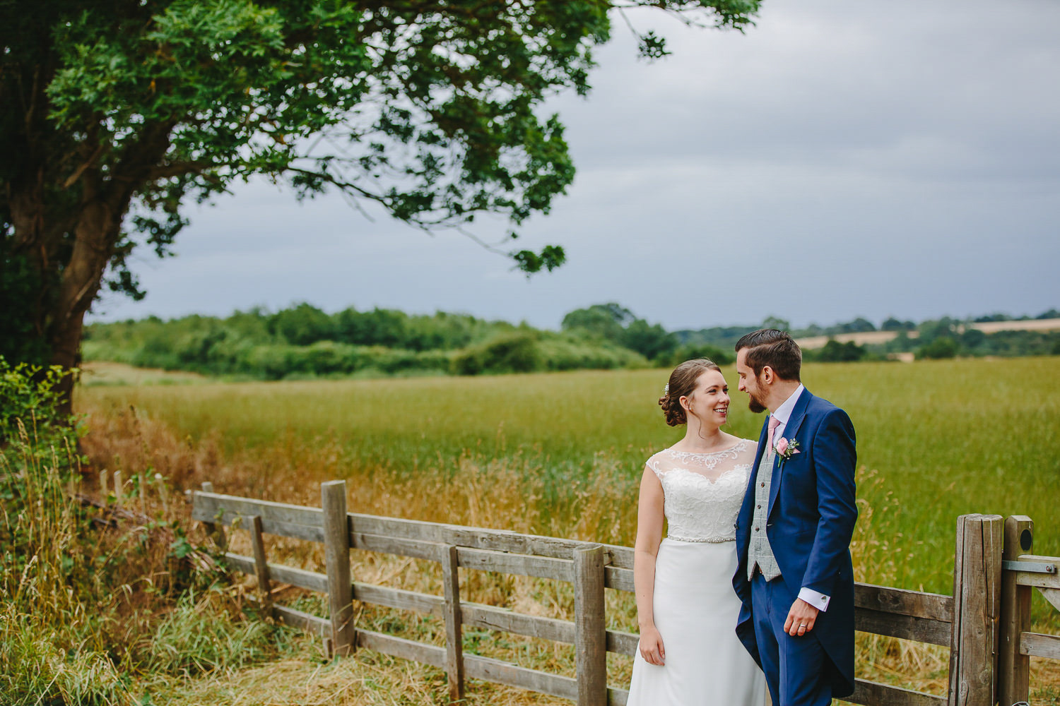 Bride and groom by a fence, near a field