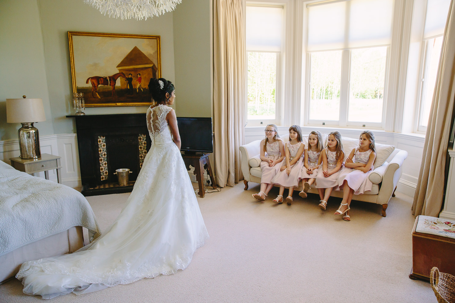 Bride standing in front of flower girls who are sitting in a row on a sofa