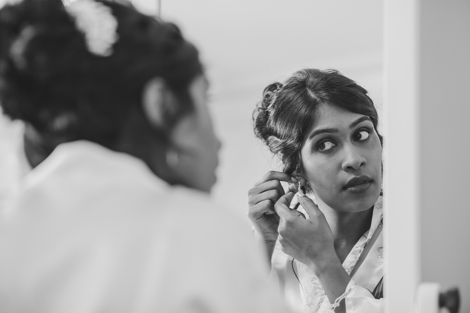 Bride putting her earrings on in front of a mirror