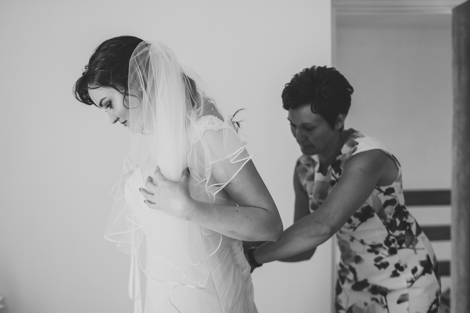 Black and white wedding photo of mum of bride helping bride into wedding dress