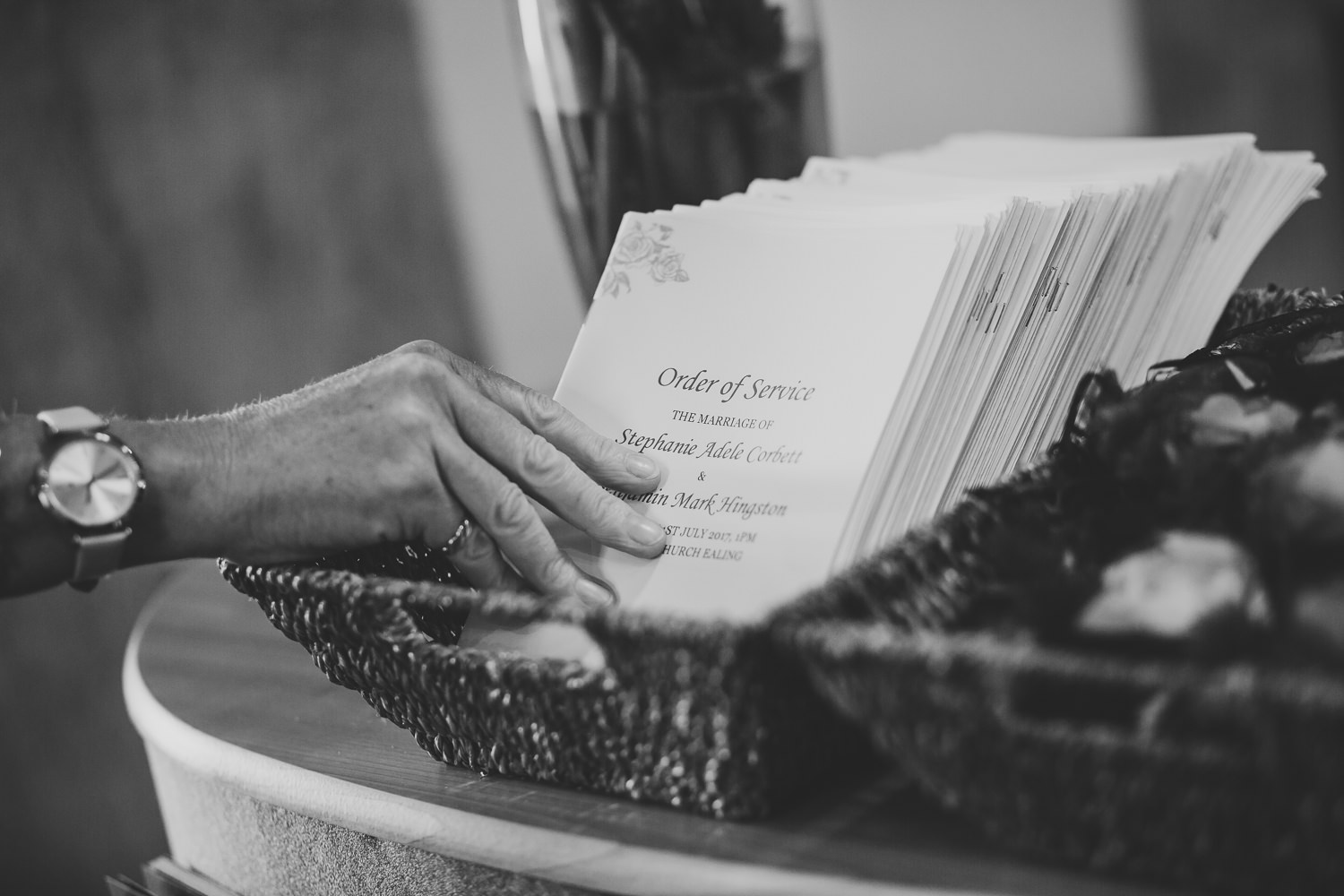 Black and white wedding photo of a hand grabbing a wedding order of service leaflet