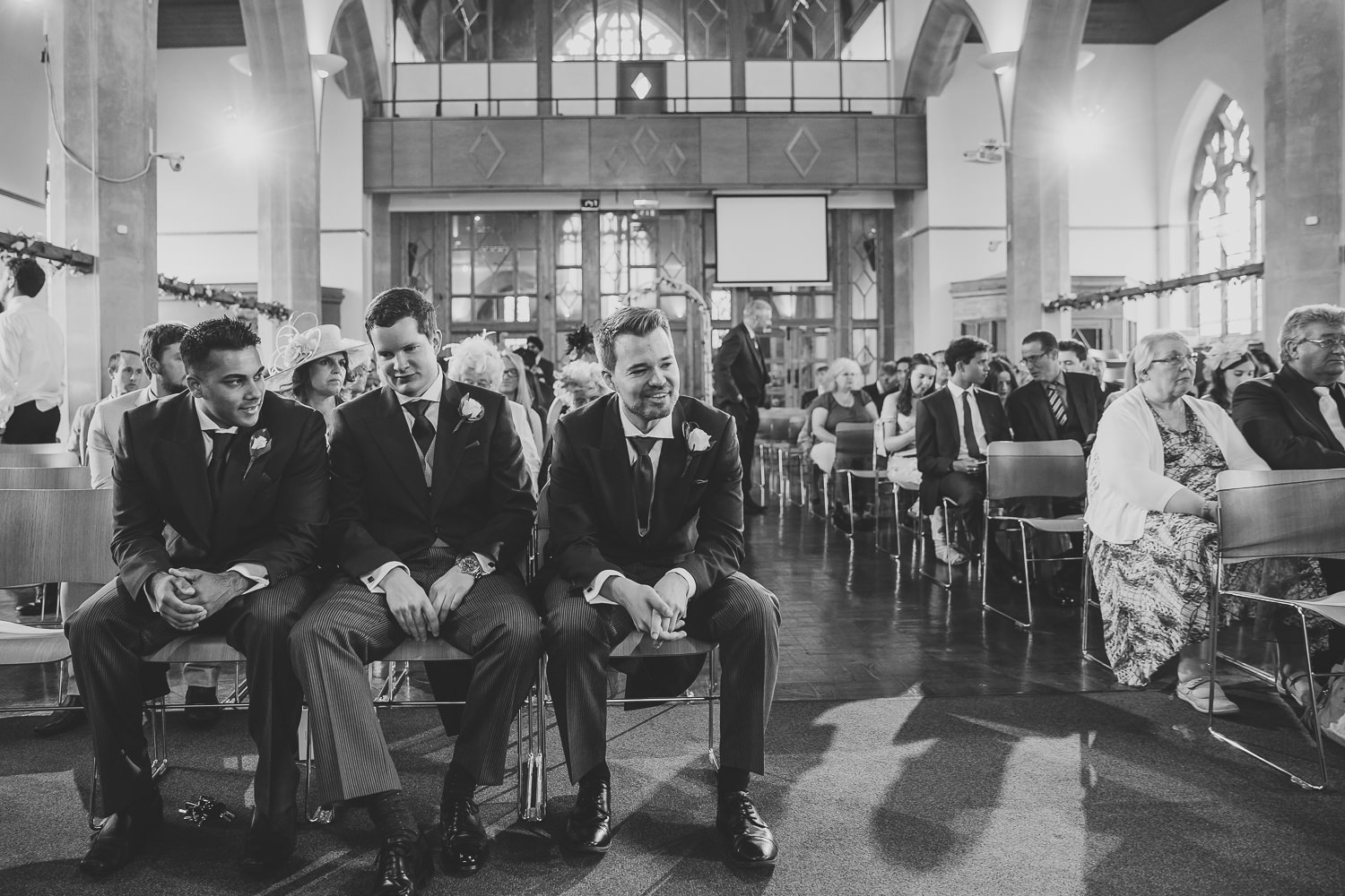 Black and white wedding photo of groom and groomsman inside a church waiting for the bride to arrive