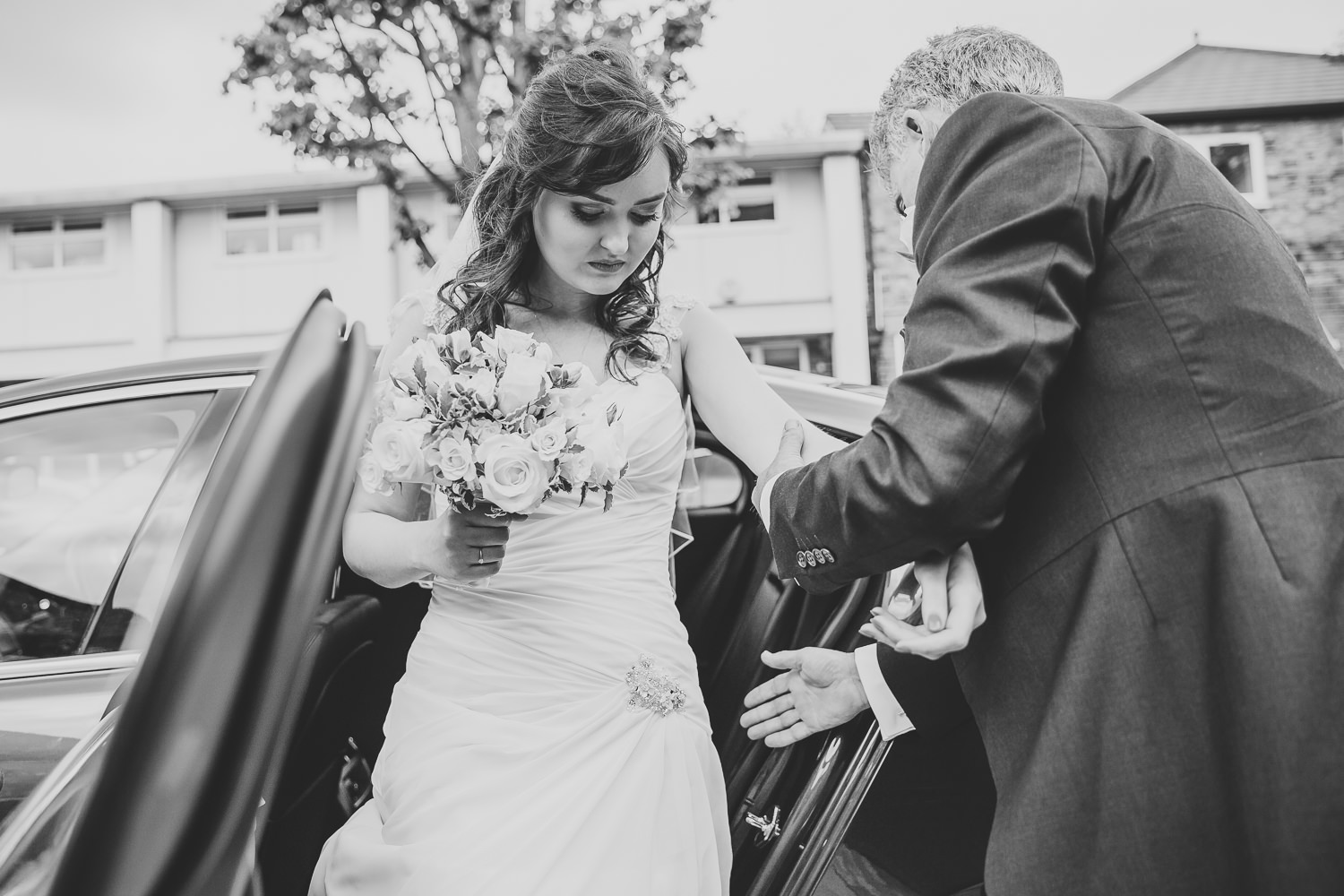 Black and white wedding photo of bride arriving for her wedding day, getting out of the car