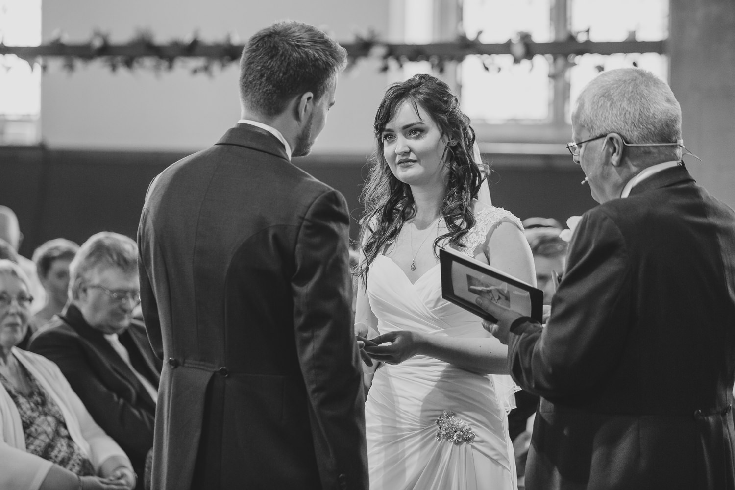 Black and white photo of a bride and groom exchanging vowels, during a church wedding ceremony