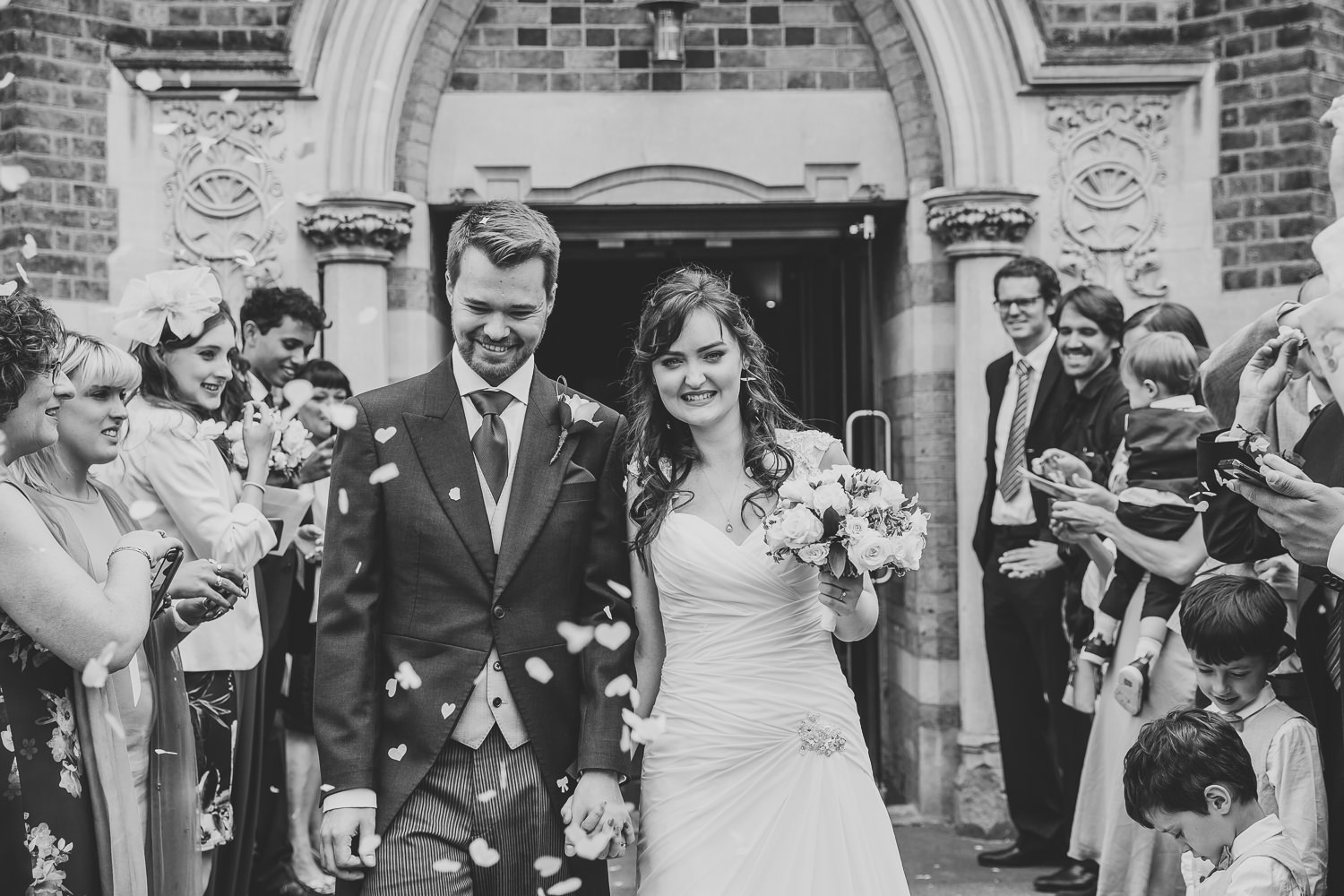 Black and white wedding photo of bride and groom walking through wedding confetti