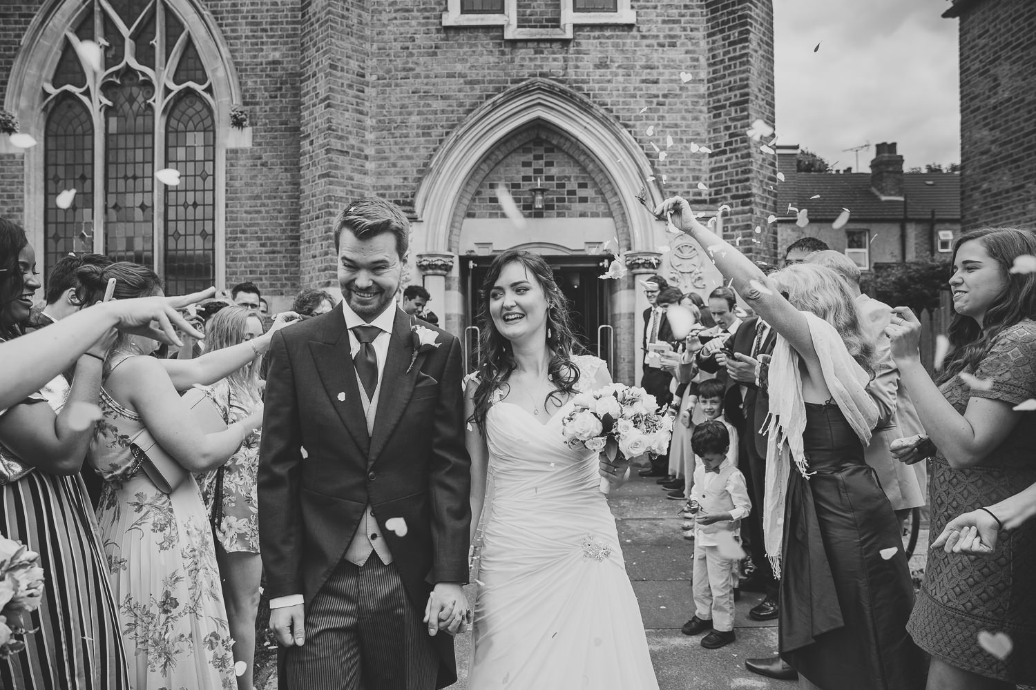 Black and white wedding photo of bride and groom walking through wedding confetti looking very happy