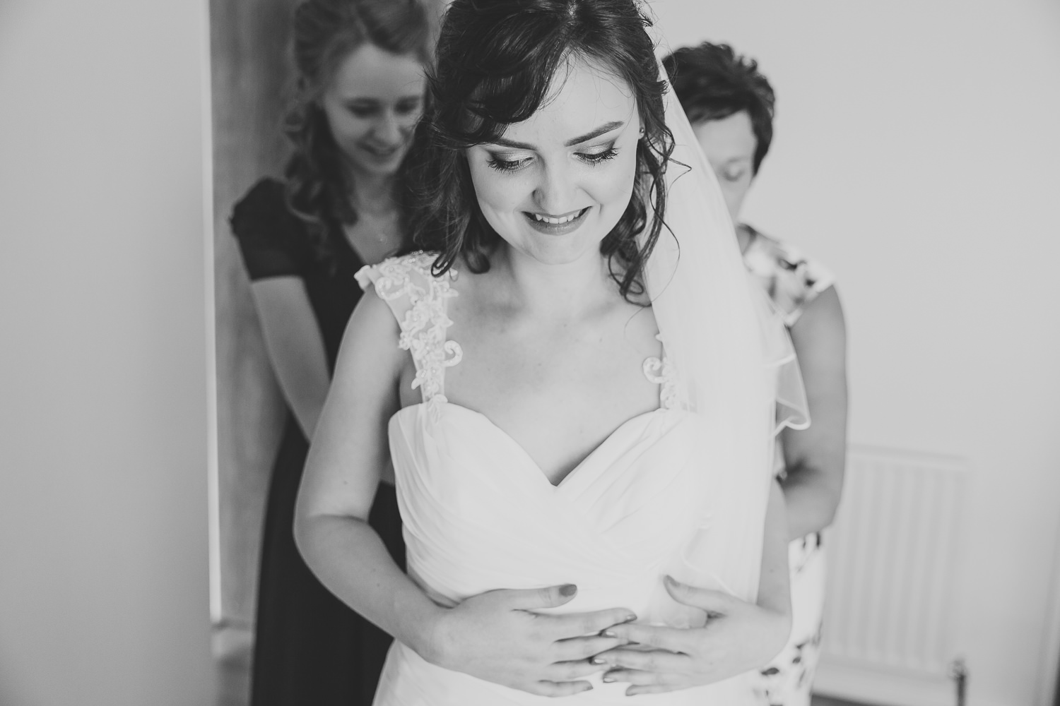 Black and white wedding photo of bride getting into her wedding dress being helped by her mum and bridesmaids