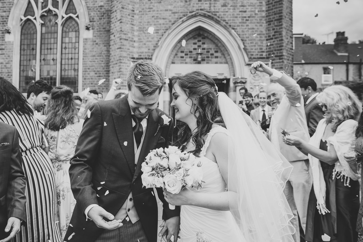 Black and white wedding photography of bride and groom walking through wedding confetti and smiling