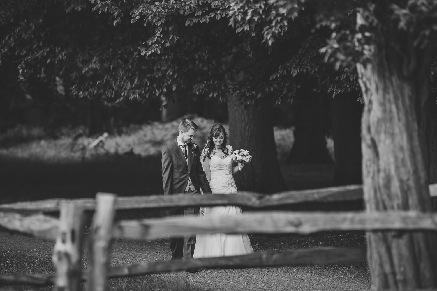 Black and white wedding photo of bride and groom walking in the park.