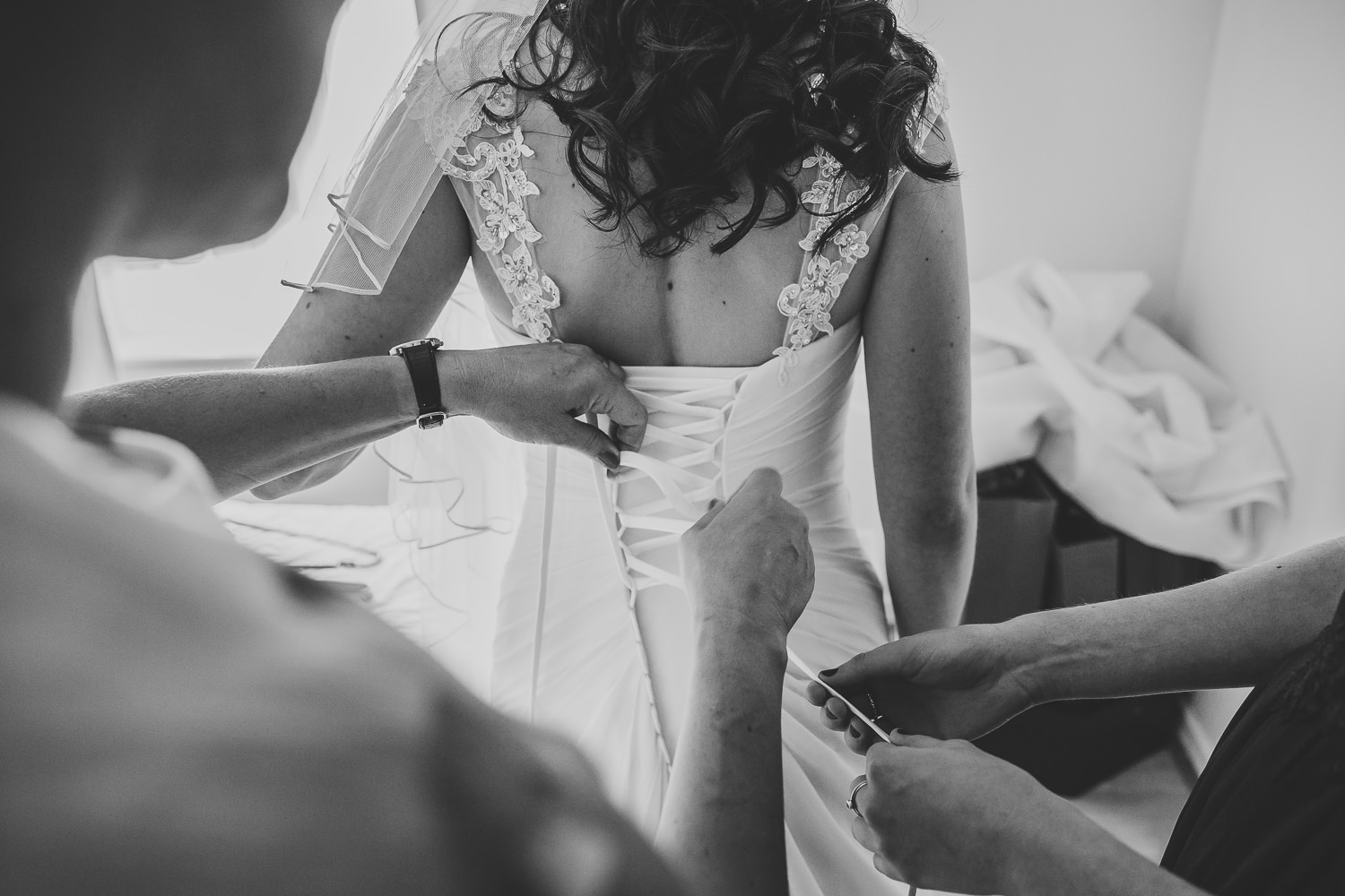 Black and white wedding photo of bride getting into her wedding dress being helped by her mum and bridesmaid