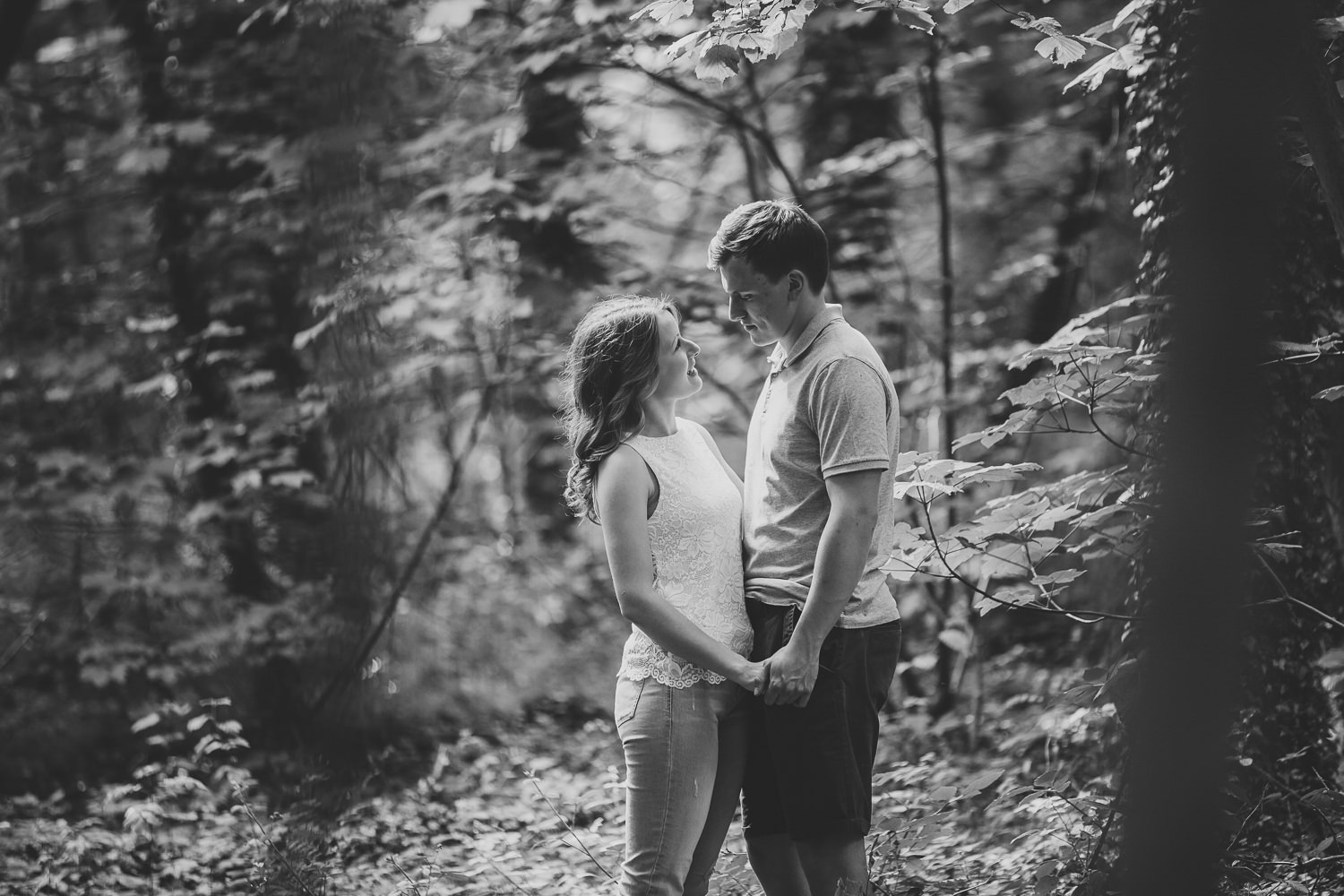 Engagement shoot photo of a couple looking at each other smiling in the woods of a country park, captured by a Cambridge Photographer
