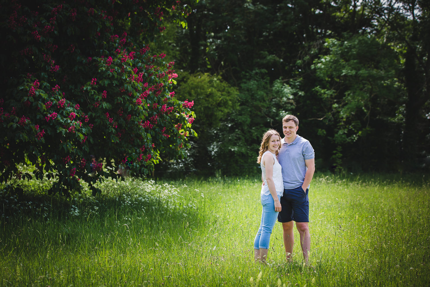 Engagement shoot photo captured by Cambridge Photographer with couple in a field in front of trees, leaves and flowers