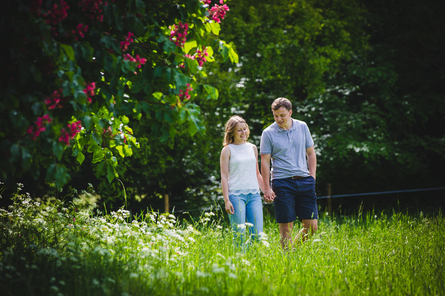 Engagement shoot photo captured by Cambridge Photographer with couple in a field walking amongst trees, leaves and flowers