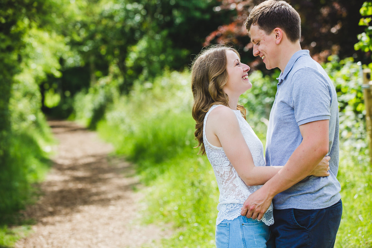 An engaged couple smiling at each other in the woodlands of Wandlebury country park Cambridge