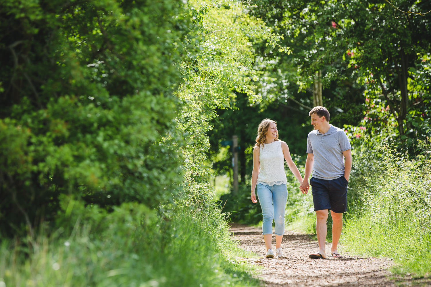 Engagement shoot photo captured by a Cambridge photographer, of an engaged couple walking along a woodland park in Summer.