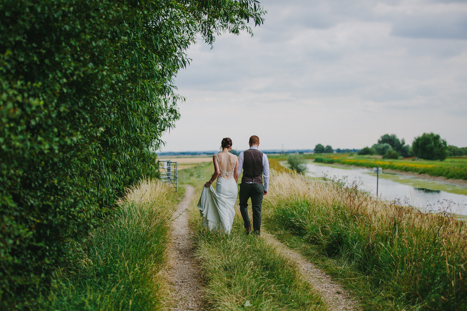 Bride and groom walking away alongside the river in Sutton, Ely, photographed by an Ely Wedding Photographer