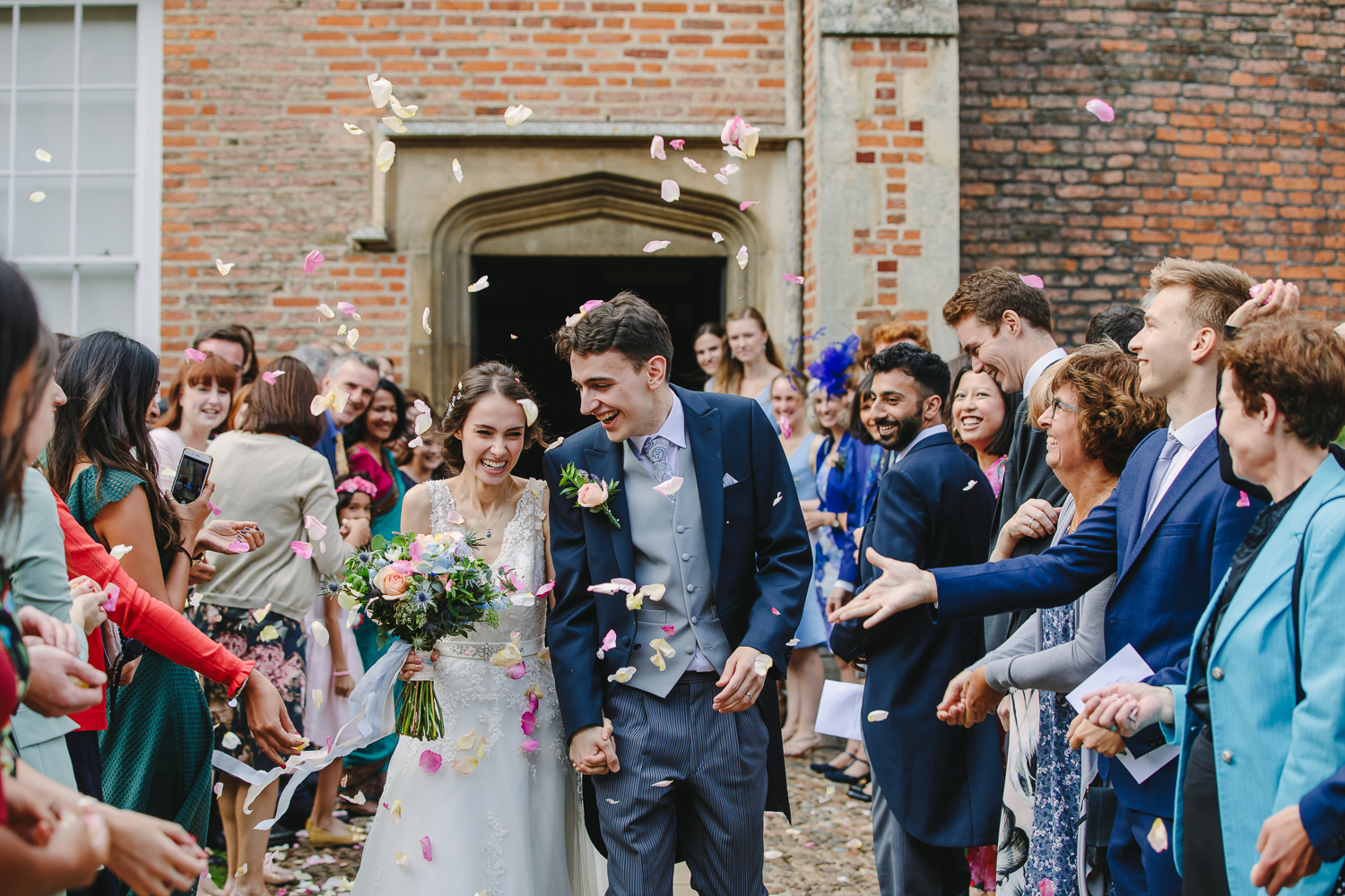 Bride and groom walking through confetti at Magdalene College Cambridge University. Photo by a Camrbridge University Wedding Photographer