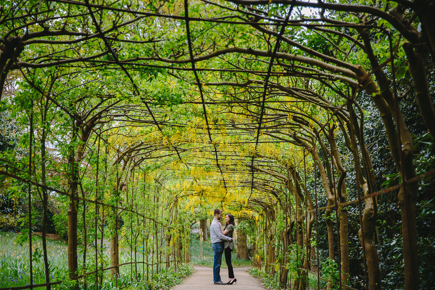 Engagement shoot photo, captured in Richmond London. Engaged couple standing underneath and archway of flowers