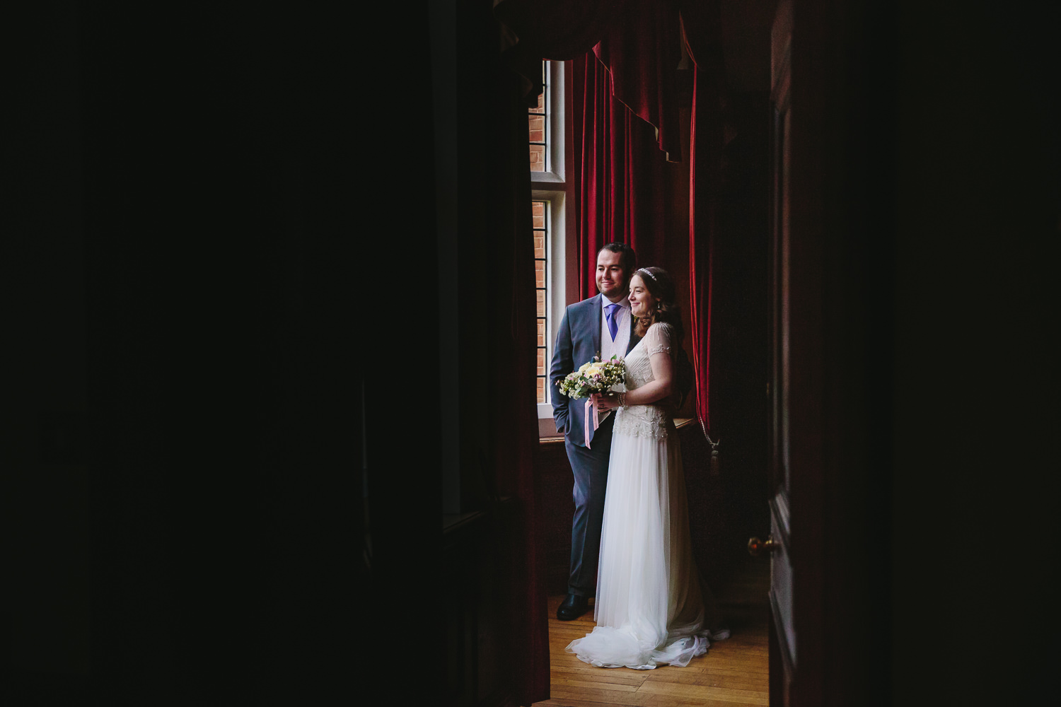 Bride and groom look through the windows inside Selwyn College Cambridge University, captured by Cambridge University Wedding photographer