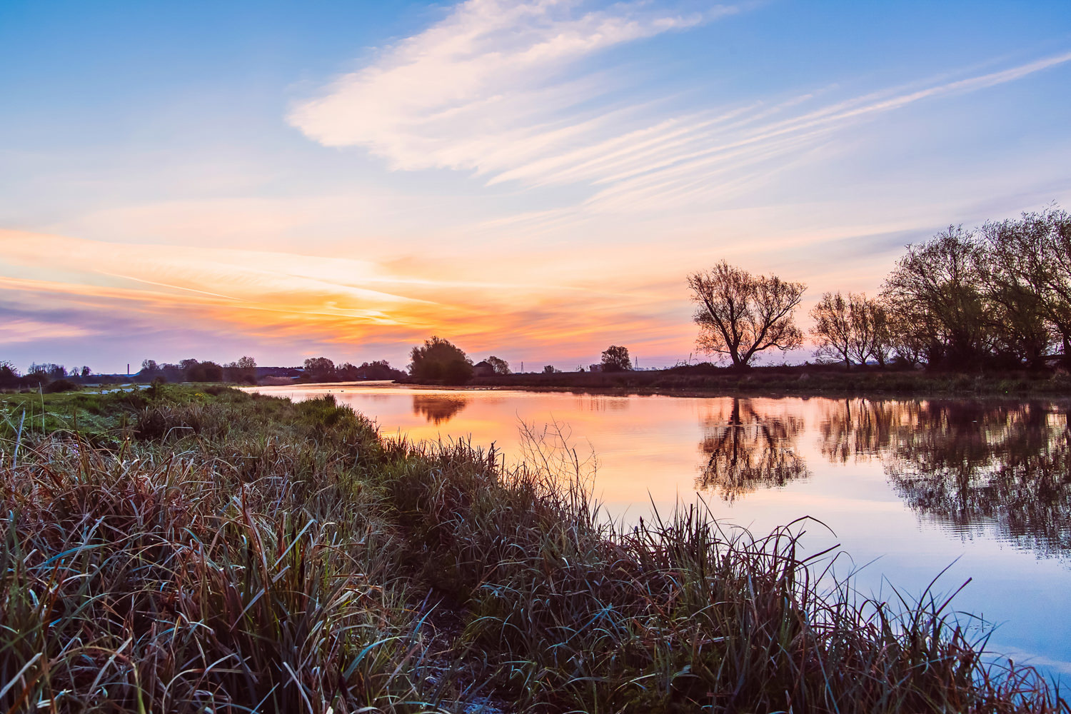 Sunrise along a river, trees in the bank in the distance